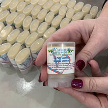 Charger l'image dans la galerie, Un tube de baume Le Petit Joufflu est tenu devant un plateau remplis d'autres tubes du baume.