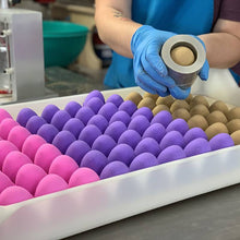 Charger l'image dans la galerie, Photos prise pendant la fabrication des bombes de bain oeufs de Pâques. La personne à la production tient le moule dans ses mains pour nous montrer la bombe de bain qui se trouve à l'intérieur.