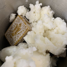 Charger l'image dans la galerie, De l'huile de noix de coco et un bloc de cire d'abeille sont placés dans un chaudron pour fabriquer les baumes.