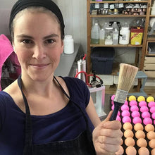 Charger l'image dans la galerie, Ariane, notre savonnière, est photographiée devant un plateau de bombes de bain de plusieurs couleurs. Elle sourit et tient un pinceau d'époussetage à la main.
