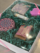 Charger l'image dans la galerie, Boîte cadeau composée de deux savons, une bombe de bain, un baume à lèvres et une petite chandelle dans un contenant métallique décoratif.
