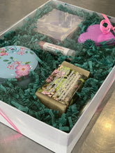 Charger l'image dans la galerie, Boîte cadeau composée de deux savons, une bombe de bain, un baume à lèvres et une petite chandelle dans un contenant métallique décoratif.