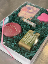 Charger l'image dans la galerie, Boîte cadeau composée de deux savons, une bombe de bain, un baume à lèvres et une petite chandelle dans un contenant métallique décoratif.