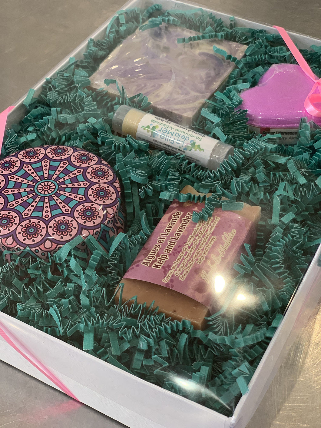 Boîte cadeau composée de deux savons, une bombe de bain, un baume à lèvres et une petite chandelle dans un contenant métallique décoratif.